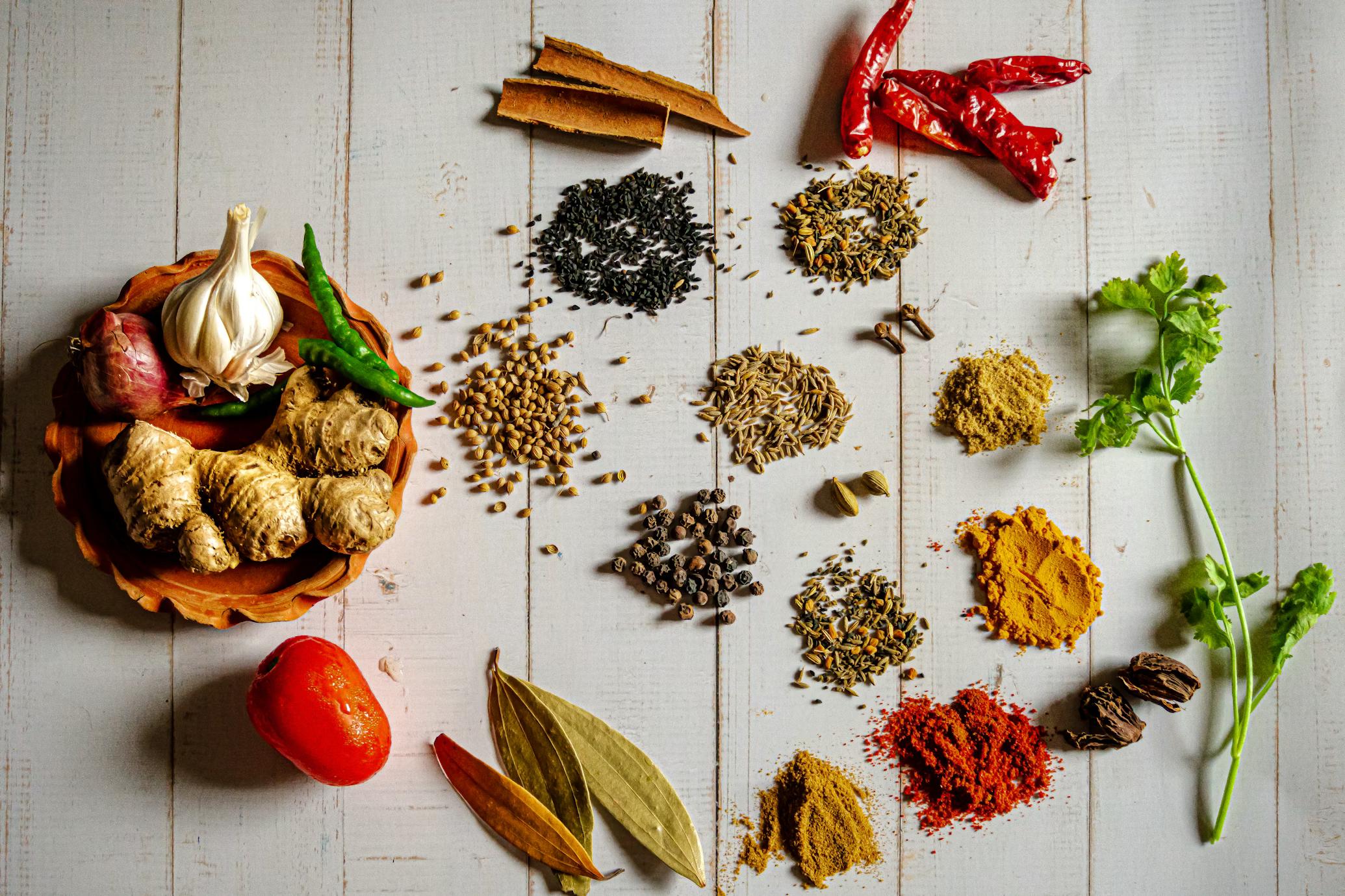 Indian spices, garlic, ginger and fresh herbs arranged on a cream wood-plank surface
